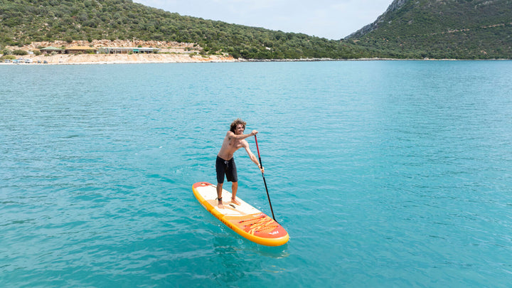 Stand-up paddling on the orange Aqua Marina Fusion SUP along a turquoise coastline