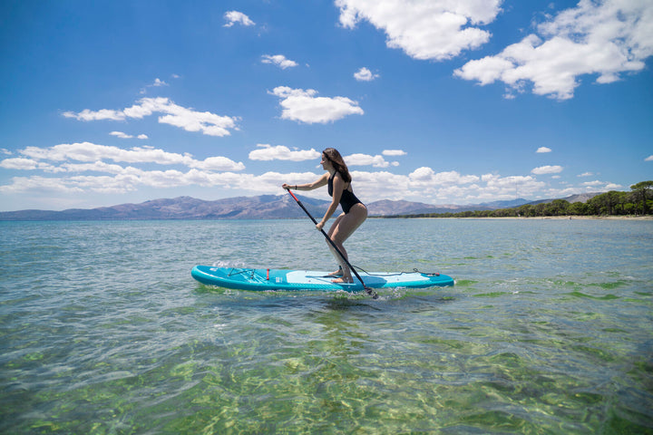 Side view of a paddler on the Aqua Marina Breeze 9'10" board in clear shallow sea water