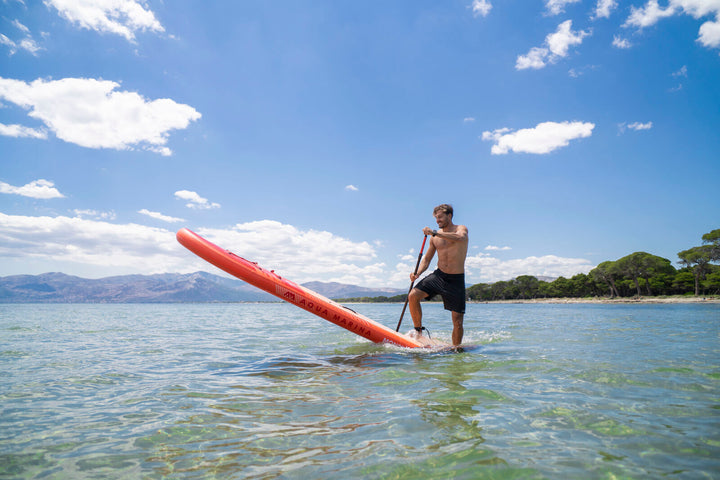 Paddler lifting the nose of the Aqua Marina Monster all-around SUP in clear shallow water
